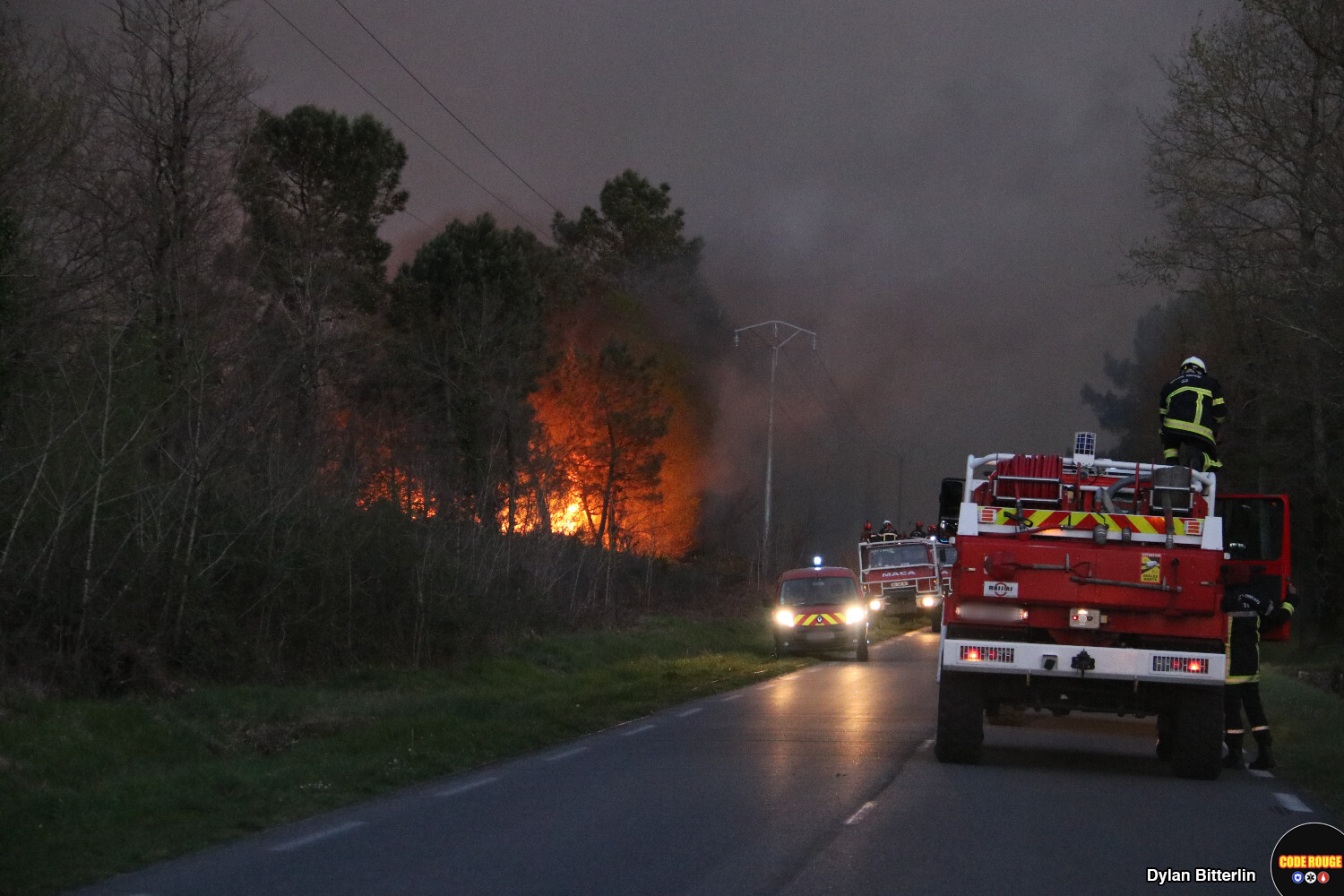 Des véhicules de sapeurs-pompiers stationnent sur une route à proximité d'un incendie de forêt