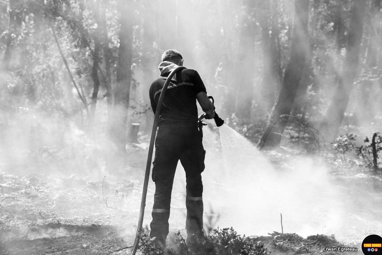 Un sapeur-pompier, de dos, répand de l'eau sur les cendres encore fumantes