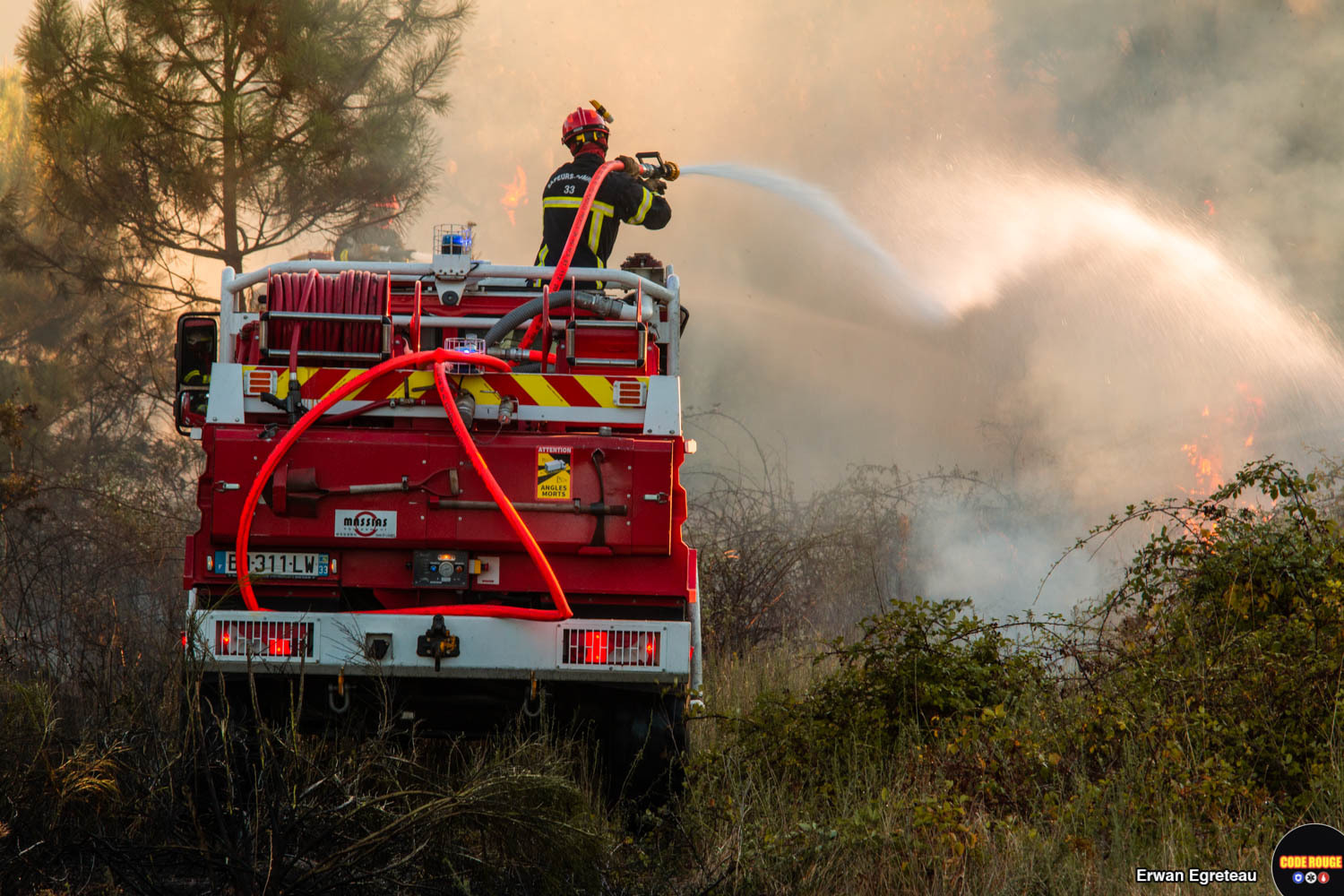 Un sapeur-pompier de dos lutte contre les flammes depuis un camion