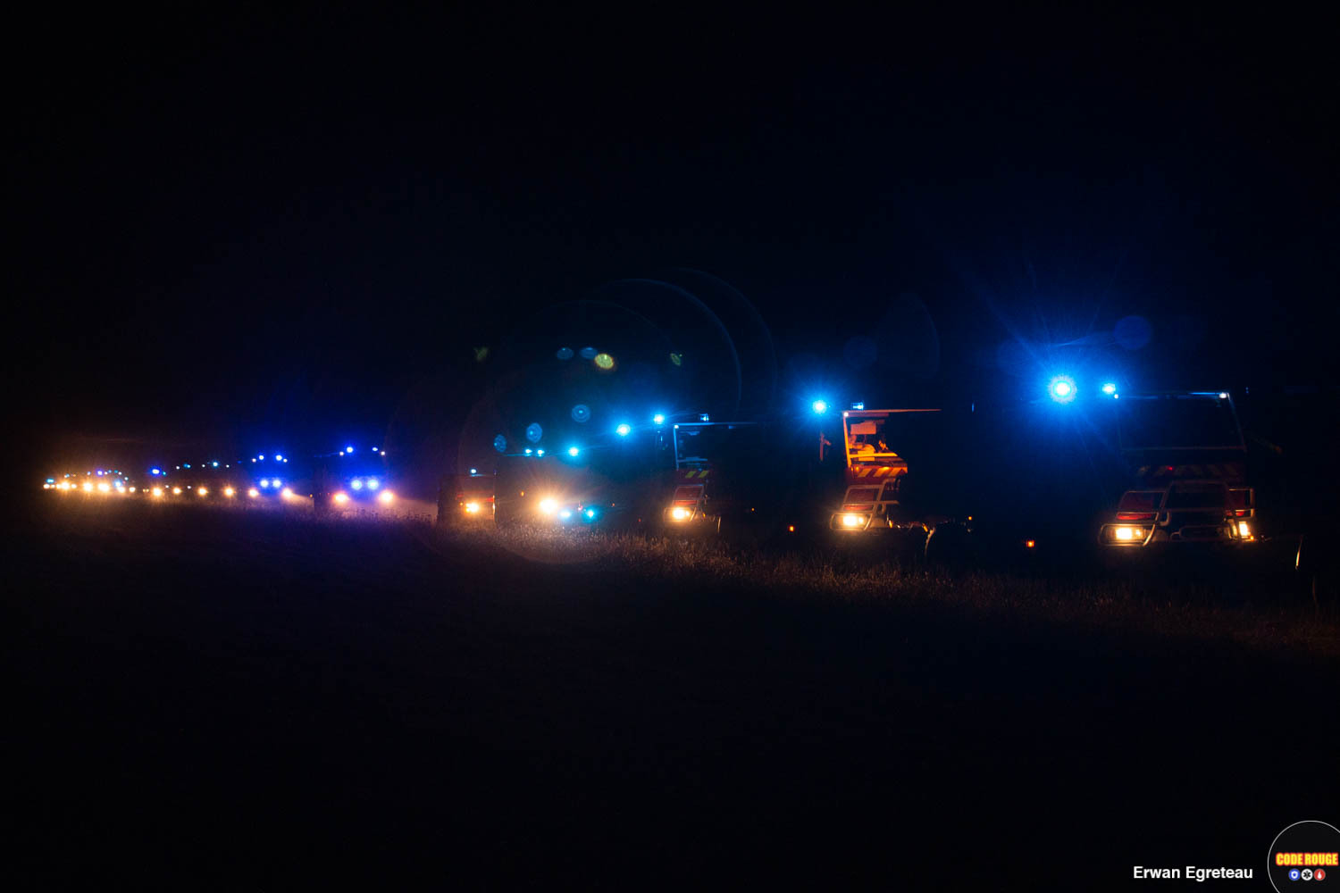 En pleine nuit, une succession de véhicules de sapeurs-pompiers circulent sur une route avec les gyrophares allumés