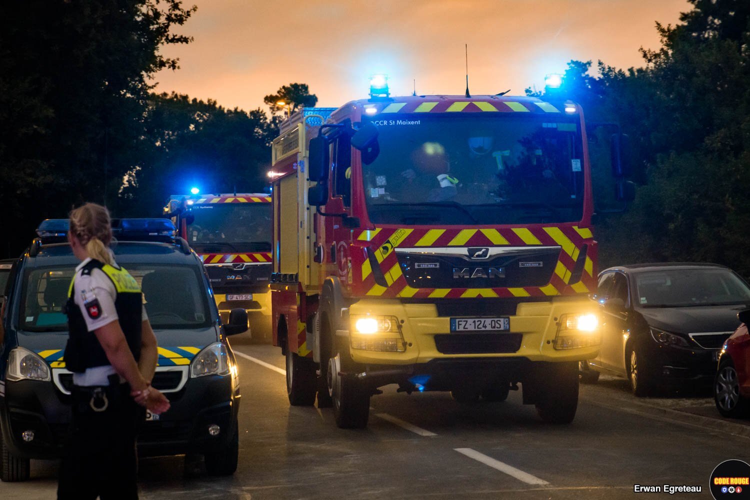 Des véhicules de sapeurs-pompiers curculent sur une route au milieu de véhicules de la police