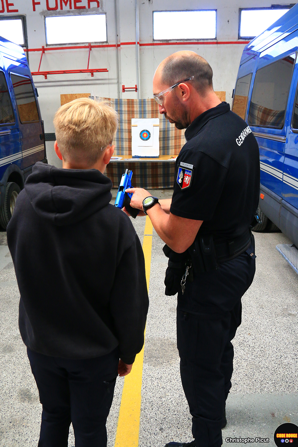 Un gendarme explique le fonctionnement d'une arme à un jeune visiteur sur un stand de tir