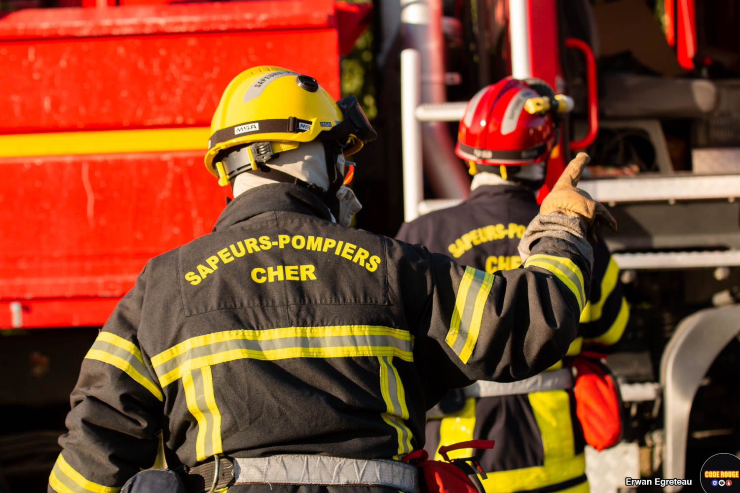 Deux sapeurs-pompiers en uniforme, de dos, marchent vers un camion
