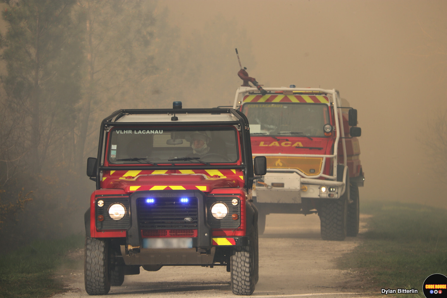 Des véhicules de sapeurs-pompiers circulent sur une route au milieu de la fumée