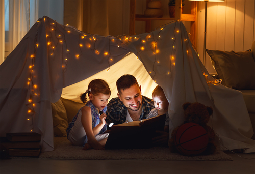 Un père lisant un livre à ses enfants dans une tente avec lampe de poche