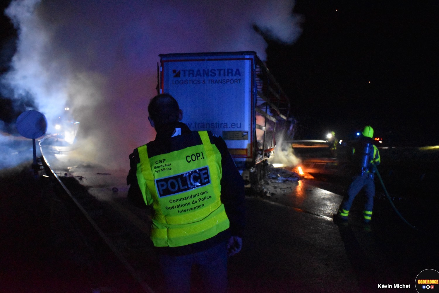 Un policier et un sapeur-pompier face à l'un des poids-lourds accidentés encore fumant en travers de la voie