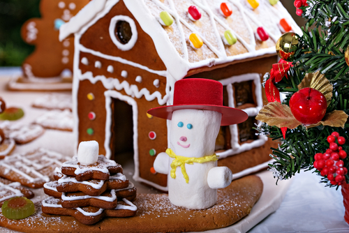 Maison en pain d’épices décorée de sucre et de bonbons, avec un bonhomme de neige en chamallow