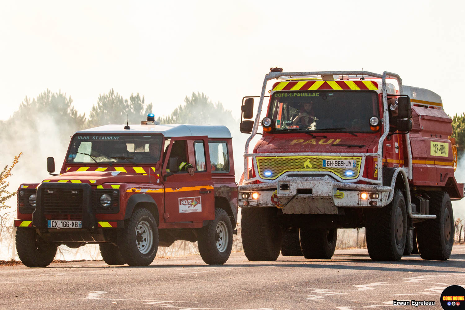 Deux véhicules des sapeurs-pompiers stationnent au bord d'une route au milieu de la fumée