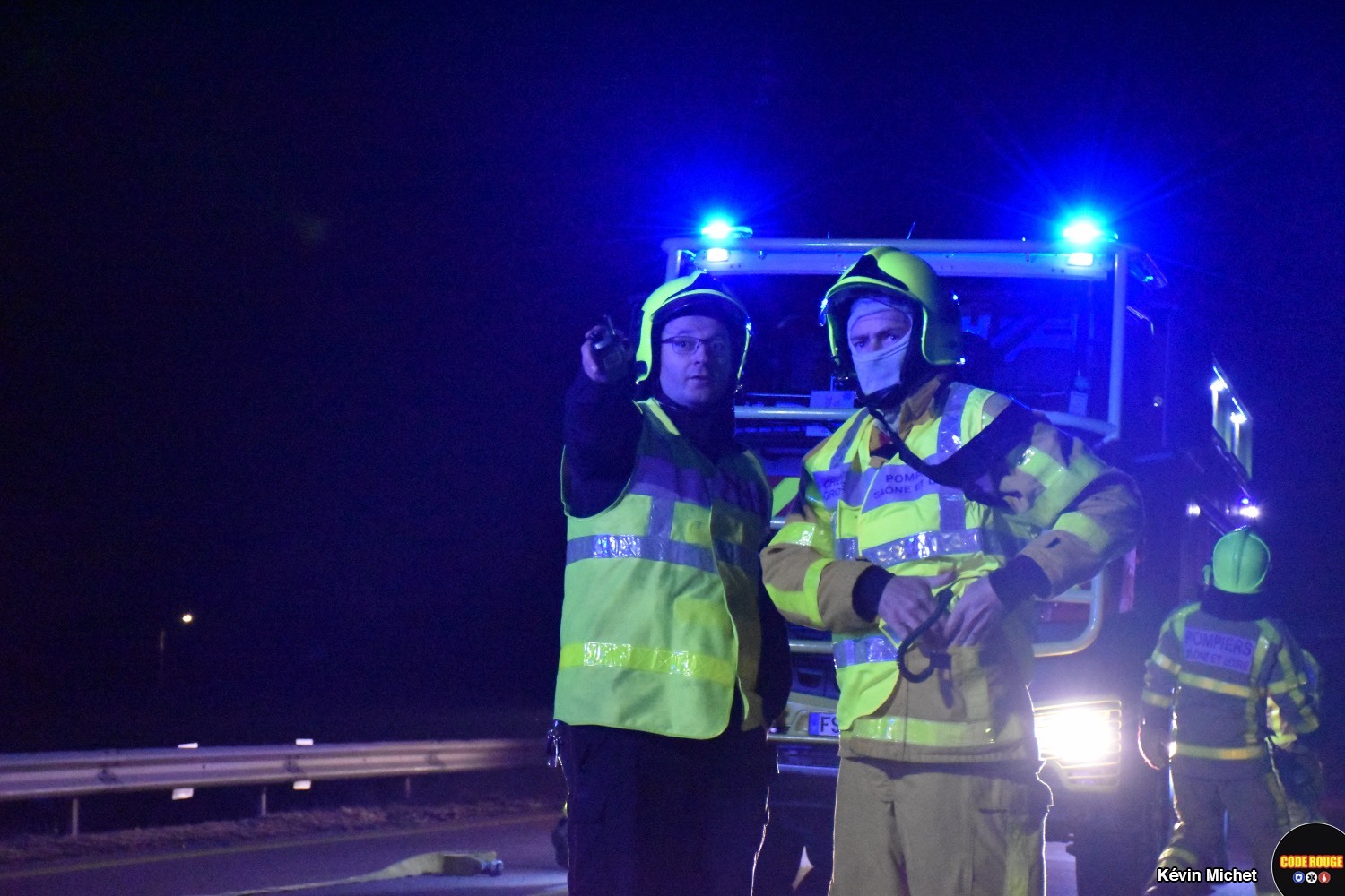Deux sapeurs-pompiers discutent en pointant du doigt le lieu de l'accident derrière le photographe