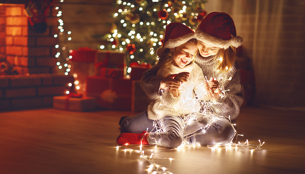 petite fille et sa maman assises sur le sol du salon, tenant une guirlande lumineuse dans les mains