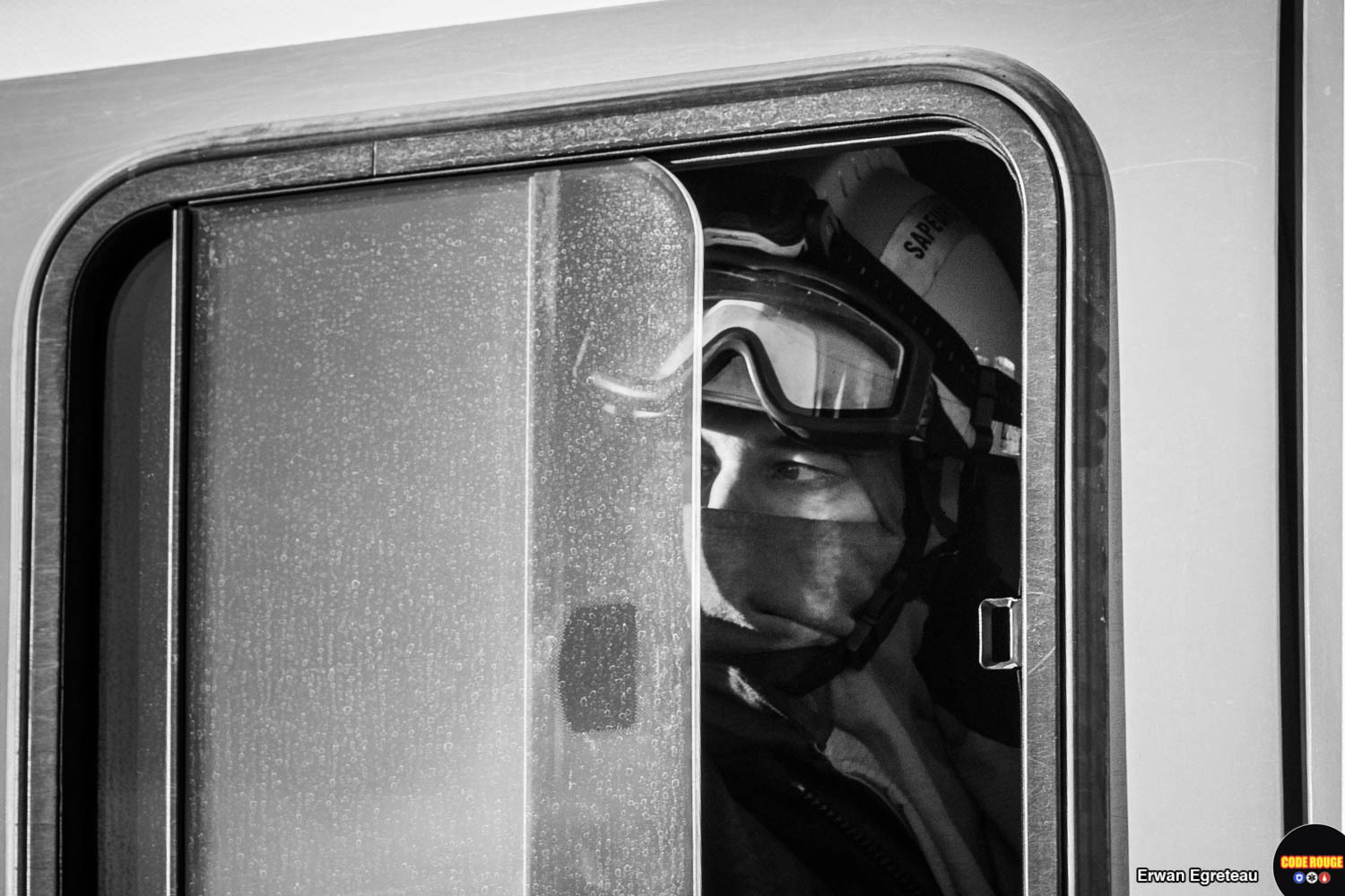 Portrait d'un sapeur-pompier regardant à travers la vitre d'un camion, le bas du visage protégé par son équipement et les lunettes de protection relevées sur son casque