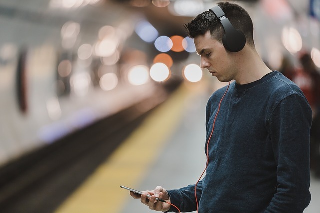 Un homme qui attend dans une station de métro avec un téléphone portable en mains et un casque