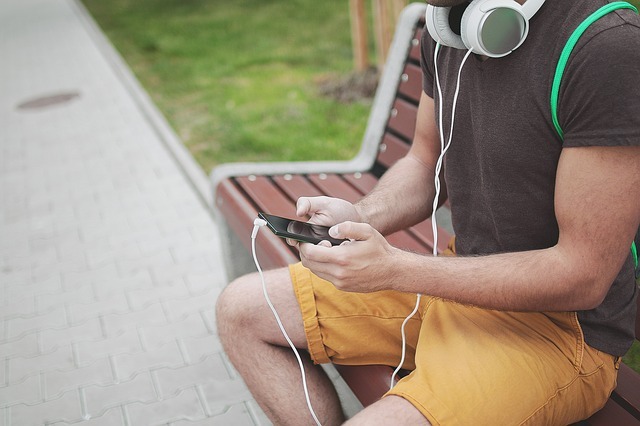 Un homme assis sur un banc avec son téléphone portable en mains et des écouteurs